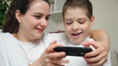 Anne ve oğlu akıllı telefondan oyun oynuyorlar. Eğlence eğlencesi, çocuk ve ebeveynlerin ortak ilgi alanları..