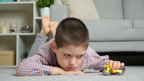 男の子は悲しいし 自宅でカーペットの上に横たわっているおもちゃのオートバイで遊んで退屈しています — ストック動画