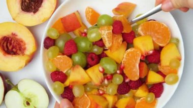 Meyve salatasını kaşıkla karıştır, şeftali, üzüm, elma, ahududu ve diğer meyvelerle karıştır..