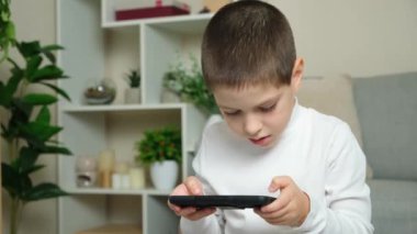 Küçük çocuk evde akıllı telefonuyla oyun oynuyor..