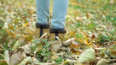 Küçük bir çocuk, sonbahar ormanında düşen sarı yaprakların üzerinde botlarıyla yürüyor..
