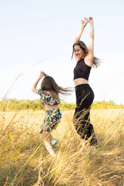 Mother and daughter have fun and dance in the summer field in nature. Mothers Day, happy motherhood and spending time together with the child.
