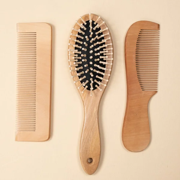 Wooden combs and hair care brush on beige background, top view.