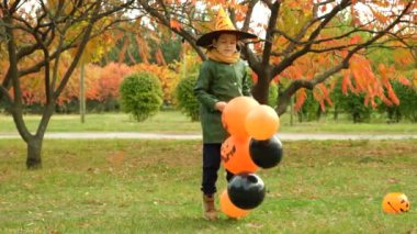 Mutlu Cadılar Bayramı çocuğu elinde bir sürü balon tutarken neşeyle parkta zıplıyor..