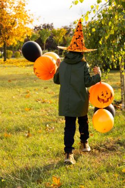Sonbahar parkında bir çocuk Cadılar Bayramı balonlarıyla yürüyor..