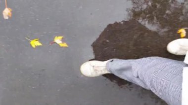 Sonbaharda yağan yağmurda, beyaz ayakkabılarla yürüyen kişinin ayakları, dikey çekim