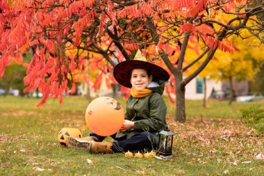 Mutlu Cadılar Bayramı çocuğu sonbaharda parkta balkabağıyla oynuyor.