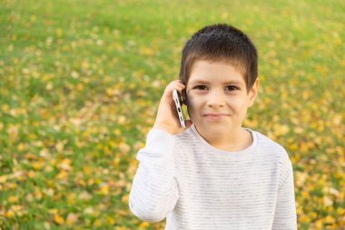 Sonbaharda parkta dururken telefonda konuşan 6 yaşında yakışıklı bir çocuk.