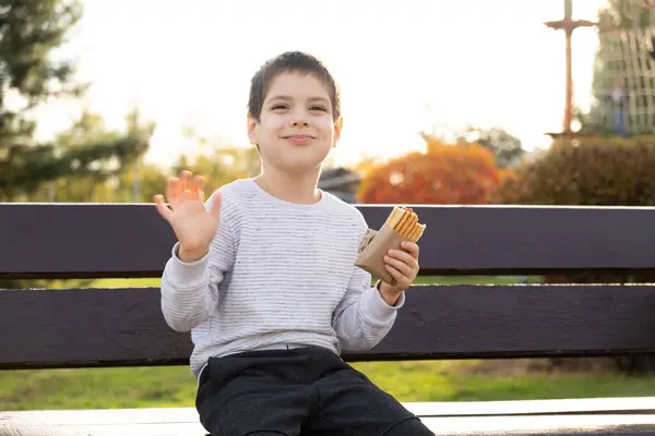 Little boy eating hot-dog and waving hello. Street Fast Food.