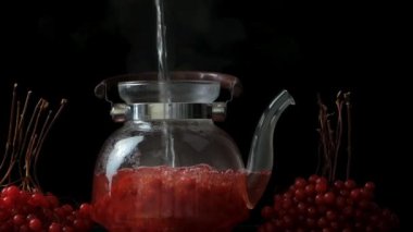 Viburnum çayı hazırlama, kaynamış su siyah arka planda viburnum üzümlü cam çaydanlığa döküldü..