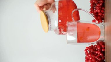 Beyaz arka plandaki çaydanlıktan sıcak viburnum çayı bir fincana dökülüyor. Vitamin çileği çayı..