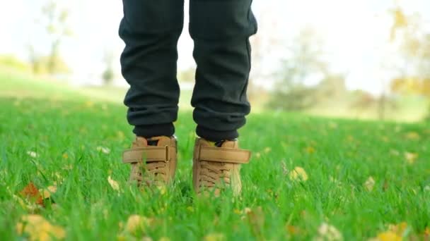 男の子は秋に茶色の靴で草の上にジャンプ 足のクローズアップ — ストック動画