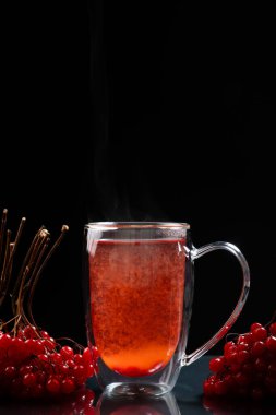 Siyah arka planda çift tabanlı cam bardakta sıcak viburnum çayı.