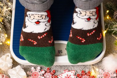 Noel çoraplı bir kadın terazinin üzerinde durur, tatillerde açgözlülükten sonra tartılır..