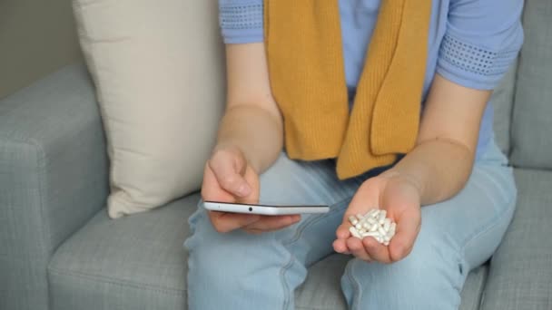 自宅でスマートフォンを使用してインターネットで薬の使用のための指示を読んでいる女性 — ストック動画