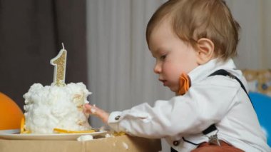 Küçük doğum günü çocuğu doğum günü pastasının üzerindeki kremaya komik bir şekilde dokunuyor..