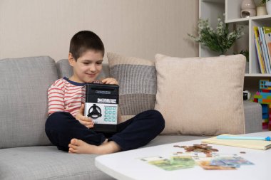 Küçük bir çocuk kumbaraya para koyuyor. Çocuklar için finansal okur yazarlık