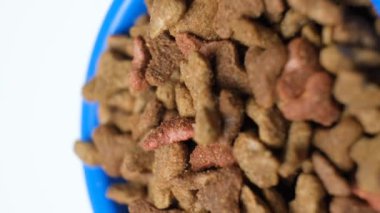 Mavi bir kasedeki kuru yavru köpek ya da kedi maması beyaz arka planda döner. Evcil hayvanlar için tam bir diyet..