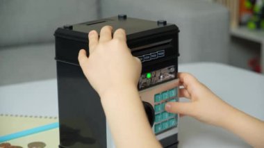 Çocuk birikmiş parayla kasayı açmak için şifre kodunu giriyor. Finansal açıdan bilgili çocuklar.