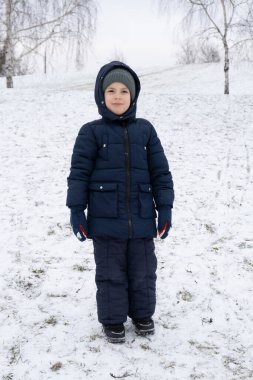 Kış mevsiminde, kar parkında mavi tulumlu altı yaşında bir çocuk..