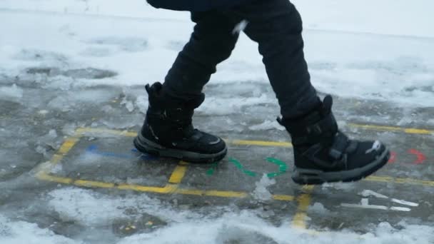 外で雪が降る時にブーツの小さな子供がジャンプします 冬のための服 子供の靴 — ストック動画