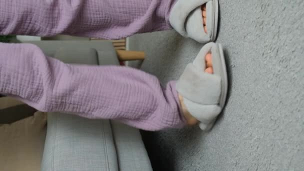 自宅でふわふわしたスリッパを着た女性がソファに座り 靴を脱いでしまう 垂直スローモーションシューティング — ストック動画