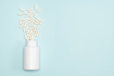 Mavi arkaplan üzerinde dağınık beyaz kapsüller ile tıbbi kavanoz metin için boşluk