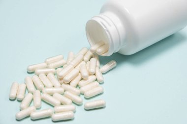 Açık mavi arka planda beyaz ilaç kapsülleri bir kavanozdan döküldü.