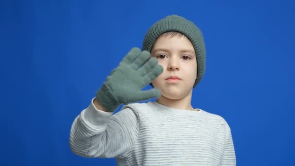 Criança Séria Triste Chapéu Malha Luvas Acenando Olá Fundo Azul — Vídeo de Stock