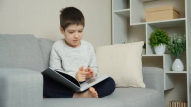 Sevimli 6 yaşında bir çocuk, kitaba bakıyor, resimlere bakıyor ve okumayı öğreniyor.