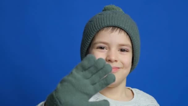 Glückliches Kind Mit Strickmütze Und Fäustlingen Die Hallo Auf Blauem — Stockvideo