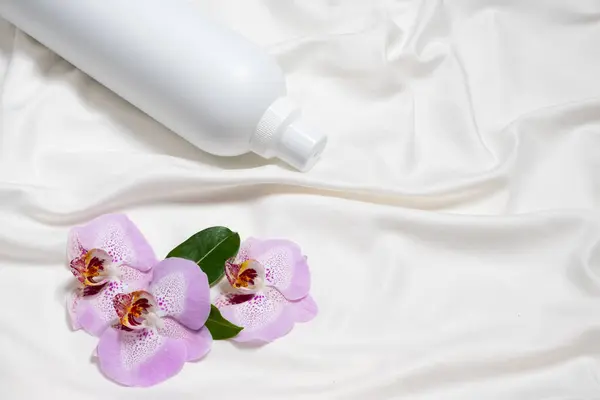 Natural fabric softener on satin fabric with orchid flowers, space for text.