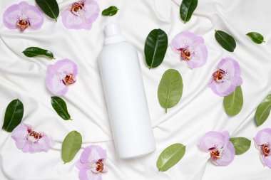 Orkide çiçekleri ile çarşaf üzerinde sıvı veya kumaş yumuşatıcısı, üst görünüm.