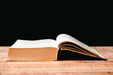 Ahşap ve siyah arka plan üzerine açık bir kitap. Nesillerin bilgeliği, bilgi ve okuma sevgisi, yazma yeri.