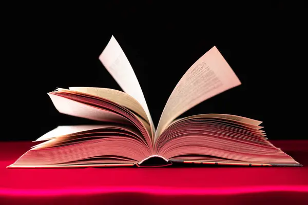 Pages of a thick book are turned on a pink and black background.