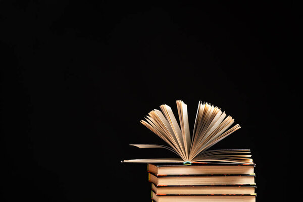 Stack of books on black background, open book, space for text