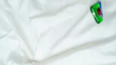 Çamaşır kapsülleri tepeden tırnağa, dikey yavaş çekimde kumaşın üzerine düşüyor