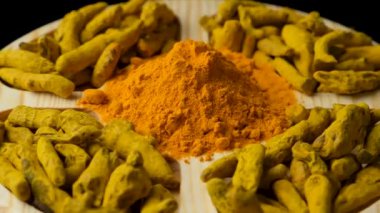 Zerdeçal tozu ve kurumuş zerdeçal kökü siyah arka planda hareket halinde.