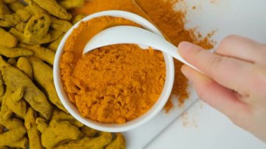 Beyaz arka planda kaşık makroda sağlıklı zerdeçal tozu, üst görünüm yavaş çekim