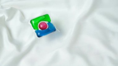 Çamaşır kapsülü yavaşça saten kumaşın üzerine düşüyor, yavaş çekim üst görünümü