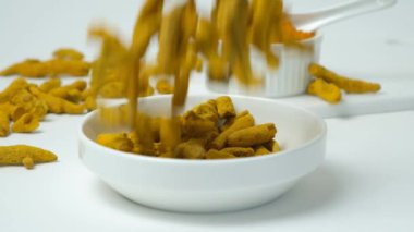 Kurumuş zerdeçal kökü beyaz arka planda yavaş çekimde plakaya düşüyor