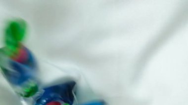 Çamaşır kapsülleri tepeden tırnağa, dikey yavaş çekimde kumaşın üzerine düşüyor