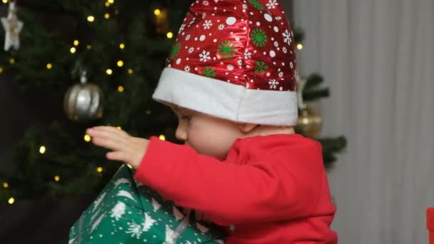 Enfant Dans Chapeau Père Noël Ouvre Des Cadeaux Près Sapin — Video
