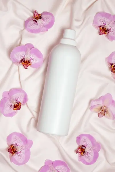 Washing liquid or fabric softener on bed linen with orchid flowers, top view.