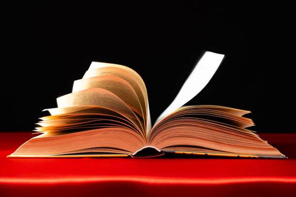 Pages of a thick book are turned on a red and black background