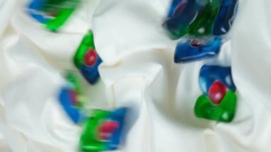 Kapsüllerdeki sıvı çamaşır deterjanı yavaşça kumaşın üzerine düşüyor, dikey ağır çekimde.