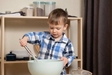 İki yaşında bir çocuk hamuru çırpıcıyla karıştırıyor. Yeni yürümeye başlayanlar mutfakta.