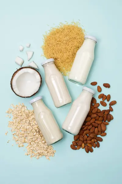 Types of plant-based milk in glass bottles. Coconut, rice, almond and oat milk on blue background