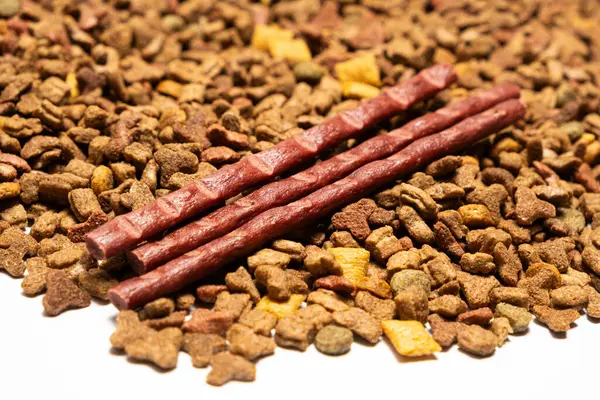 Treats for cats meat sticks sausages against the background of dry food. Complete diet for adult cats.