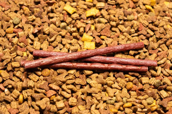 Treats for cats meat sticks sausages against the background of dry food. Complete diet for adult cats.
